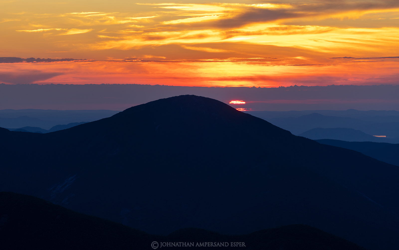 Summer sun disk setting behind Algonquin Peak, seen from Mt Marcy ...